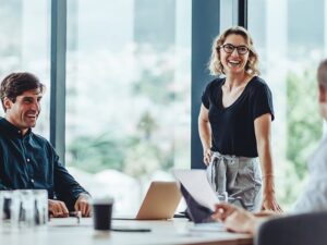 Profissionais em uma reunião de negócios em um ambiente moderno, com uma mulher sorridente liderando a apresentação. Esse cenário reflete a atmosfera colaborativa e eficiente que você pode encontrar ao organizar eventos no melhor hotel para eventos em Foz do Iguaçu.